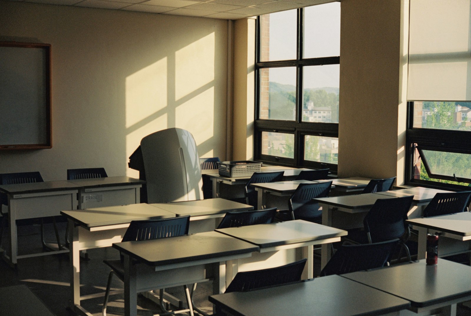 Rows of empty desks in afternoon light through tall classroom windows — the room two teaching days a day are lost from.